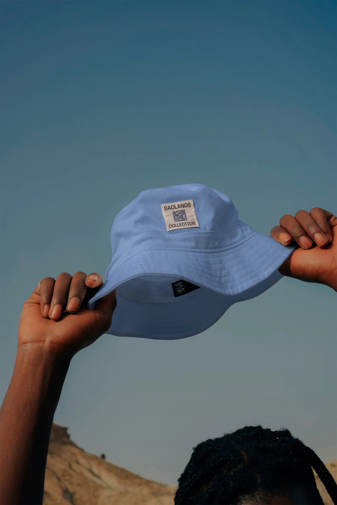 Bucket hat mock-up taken by a person with his two hands and a blue sky behind