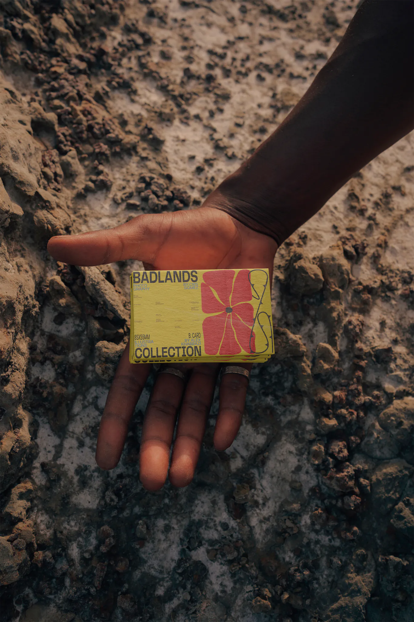 A palm of a hand from a dark-skinned guy holding a business card mock-up over a rocky surface
