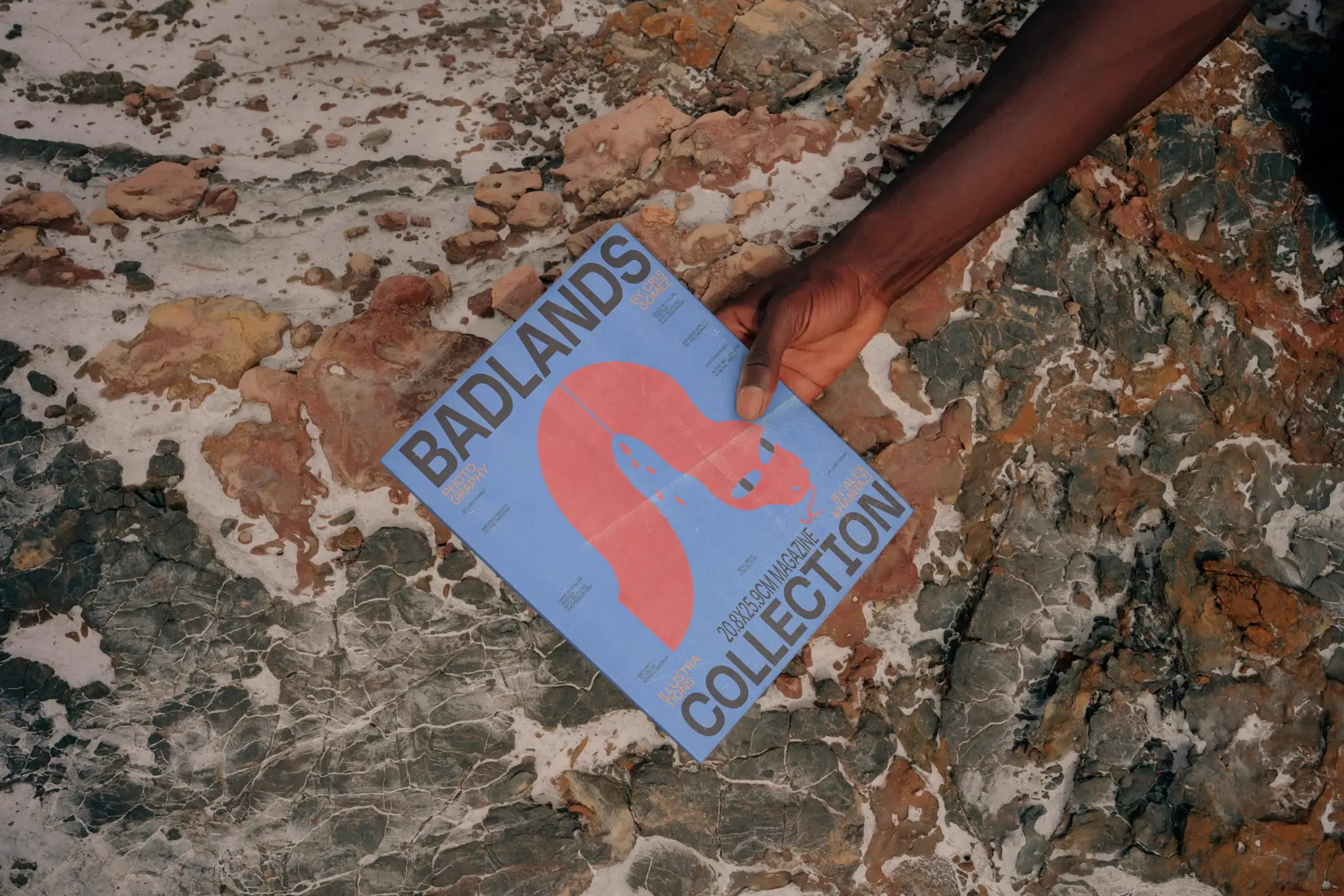 A hand from a black guy holding a magazine mock-up over a rocky surface