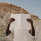 Black man holding an open magazine mock-up in a desert environment with a blue sky behind