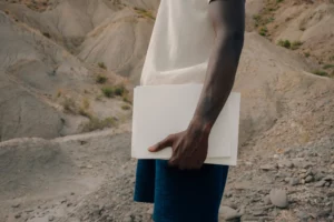 Dark-skinned person holding several magazine mock-ups in a desert environment