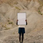 Black guy holding a framed poster mock-up in a desert environment