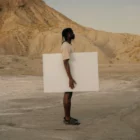 Dark-skinned person holding a poster mock-up in a desert environment