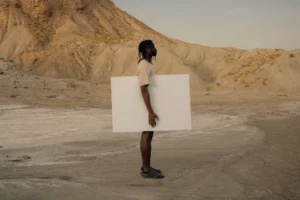 Dark-skinned person holding a poster mock-up in a desert environment