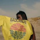Young african-american person from behind holding a t-shirt mock-up with his arm in a desert environment