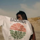 Young african-american person from behind holding a t-shirt mock-up with his arm in a desert environment