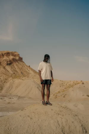 Black guy wearing a t-shirt mock-up while he is standing on a mound in a desert environment