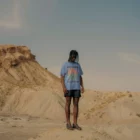 Black guy wearing a t-shirt mock-up while he is standing on a mound in a desert environment