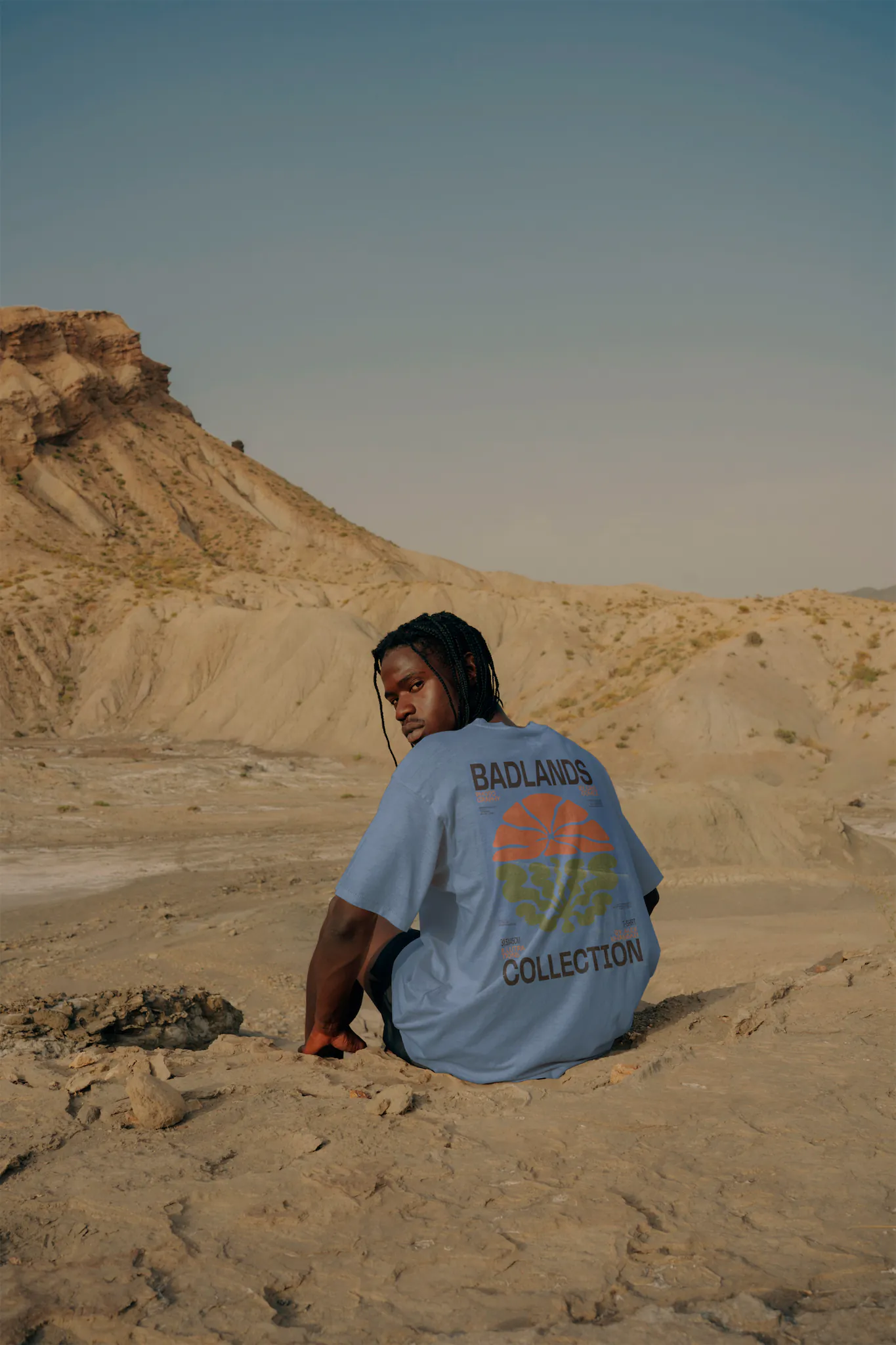 Black guy from behind sitting and wearing a t-shirt mock-up in a desert environment