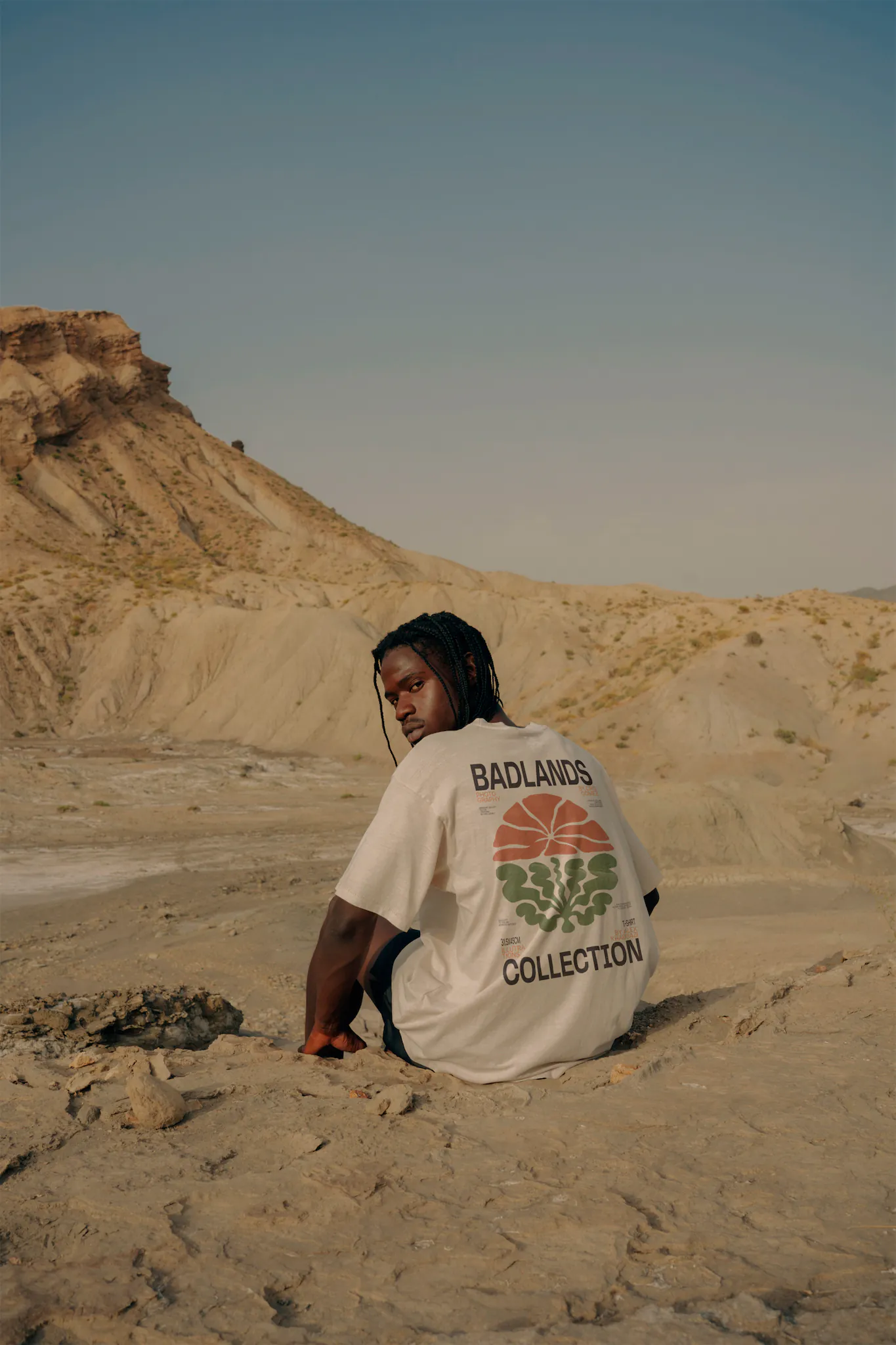 Black guy from behind sitting and wearing a t-shirt mock-up in a desert environment