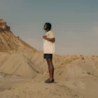 Dark-skinned person wearing a tote bag mock-up on top of a mound in a desert environment