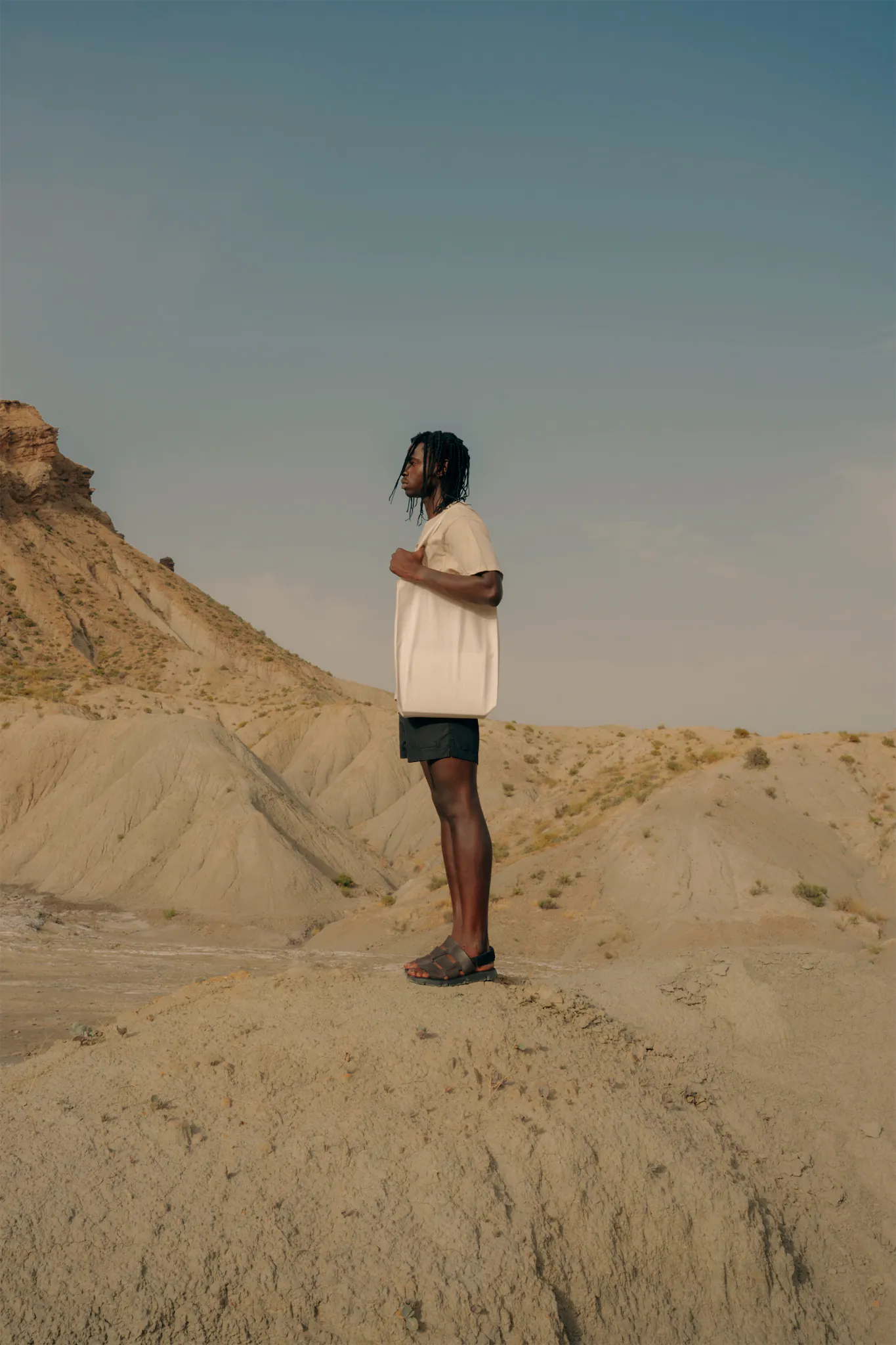 Dark-skinned person wearing a tote bag mock-up on top of a mound in a desert environment