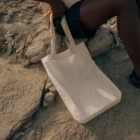 Tote bag mock-up on a rocky surface next to a dark-skinned person who is sitting next to it