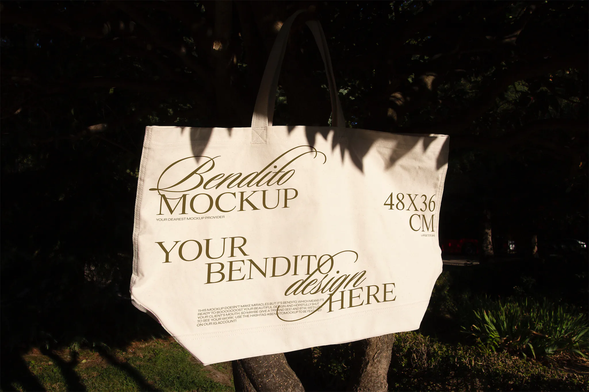 Tote bag mockup freebie hanging from the branch of a tree.