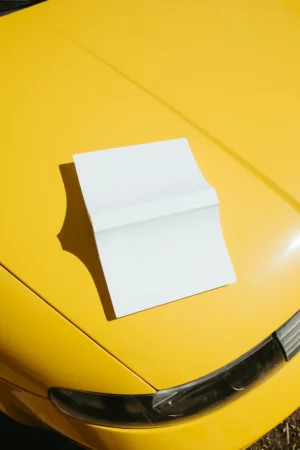 Paperback book mockup on a yellow car surface.