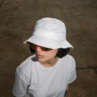 Bucket hat and t-shirt mockup worn by a female model with sunglasses in the street.