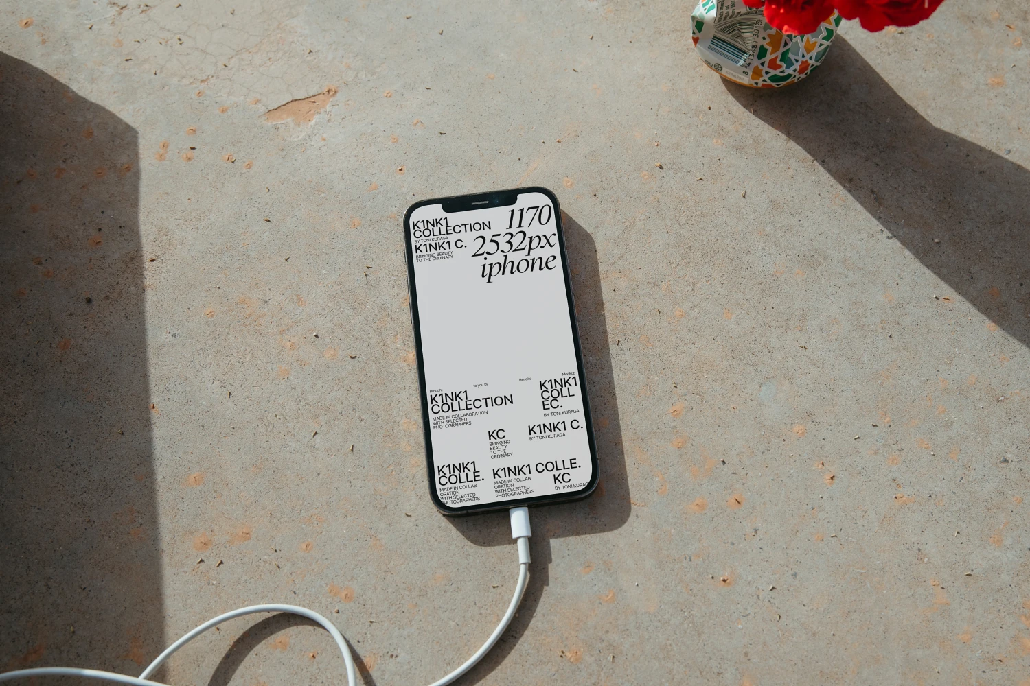 iPhone mockup placed on a urban floor. It is surrounded by its charge wire and flowers.