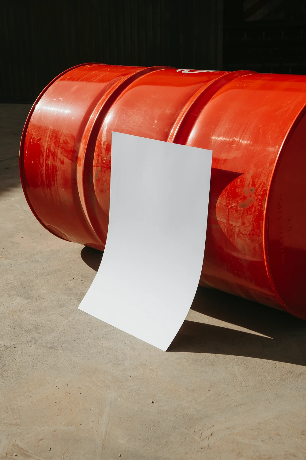 Creative poster mockup placed in the groundfloo against a red rusty barrel. The image has vertical orientation.