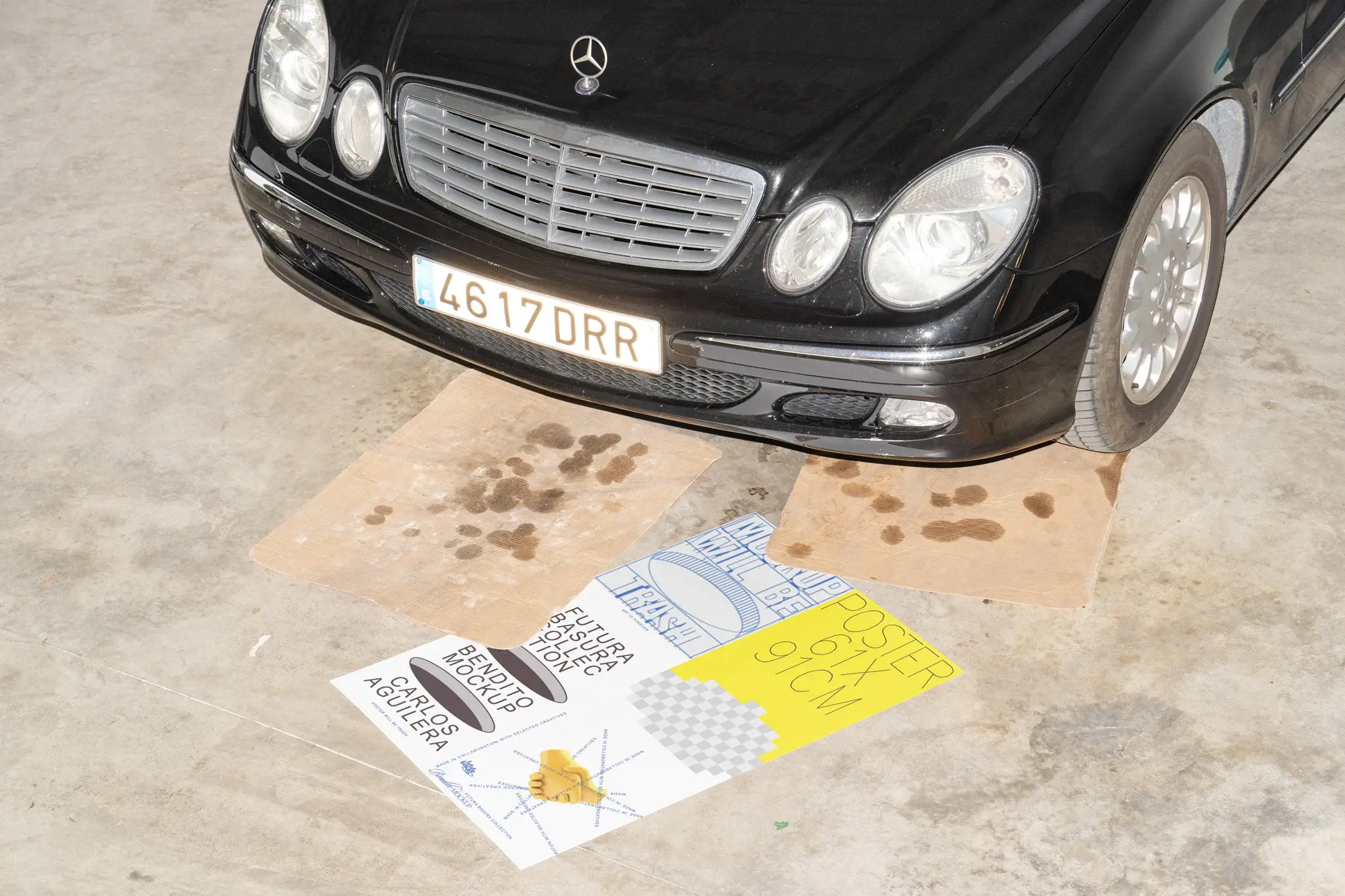 Poster mockup on the floor with 2 dirty cardboards on top in front of a luxury car