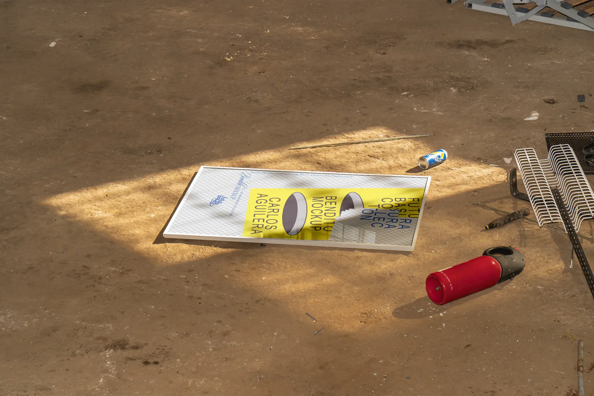Framed poster mockup on the ground next to a red extinguisher and a blue can