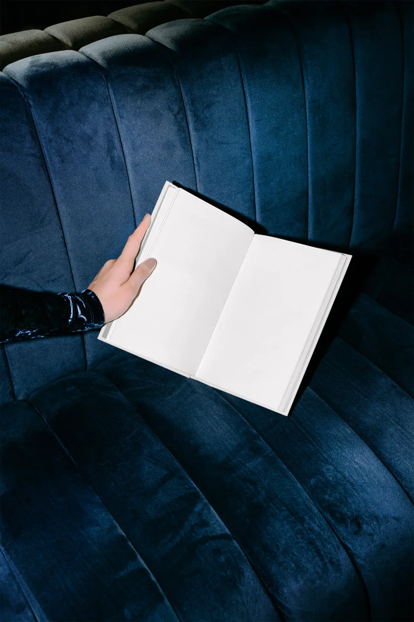 Open book mockup holded by a feminine hand dressed on an fancy blouse on top of a fancy blue couch