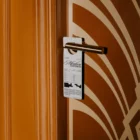 Door hanger mockup which is hanging from the doorknob of an orange door with patterns