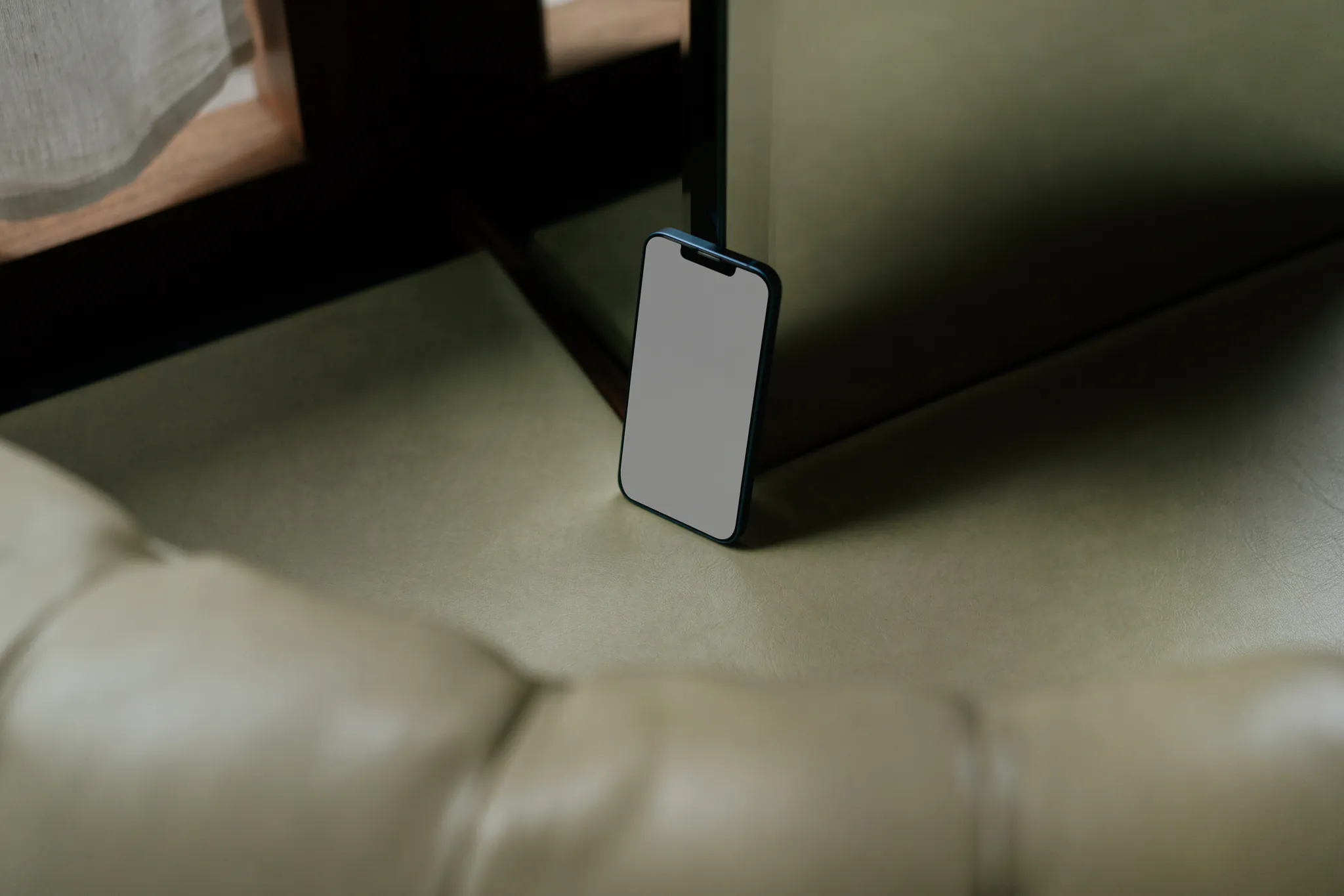 Iphone mockup behind a green leather couch next to a mirror