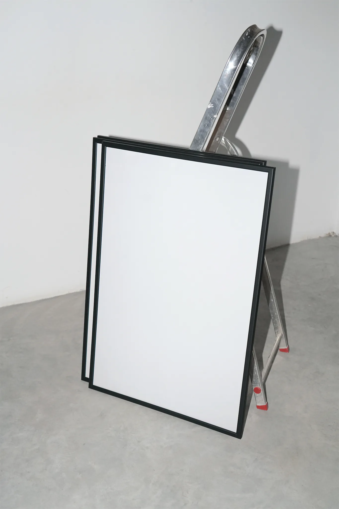 Set of framed poster mockups leaning against a ladder in a room with white walls and concrete floor