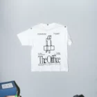T-shirt mockup hanging on a wall with one of its sleeves open and the other one closed next to an office table with papers on top
