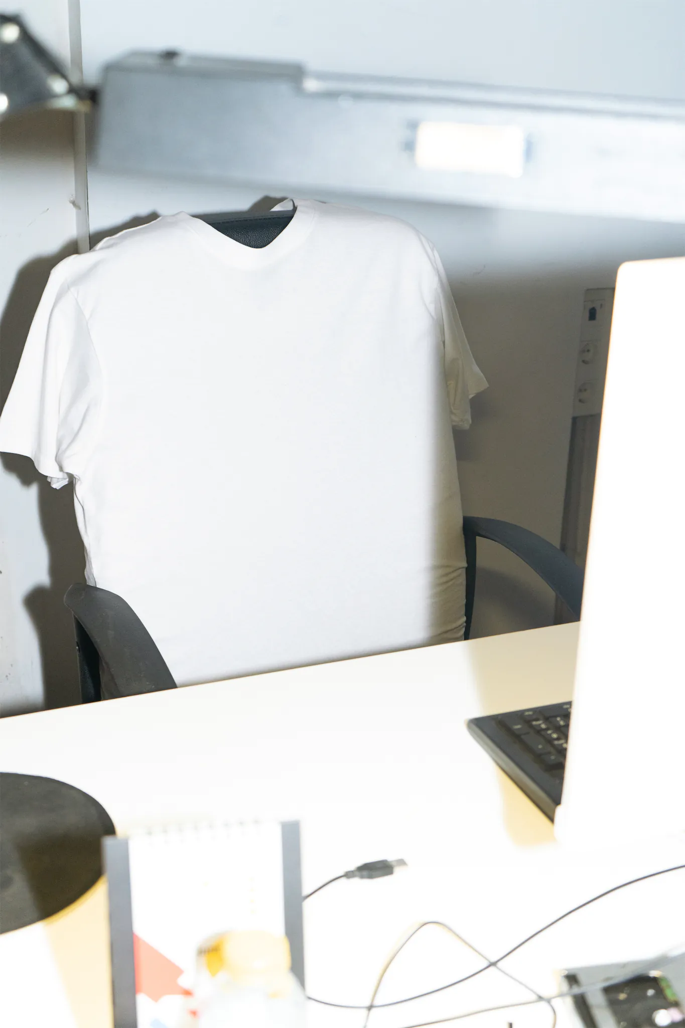 T-shirt mockup over the back of an office chair in front of a laptop