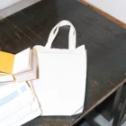Tote bag mockup on top a brown metal table next to an open book and magazines