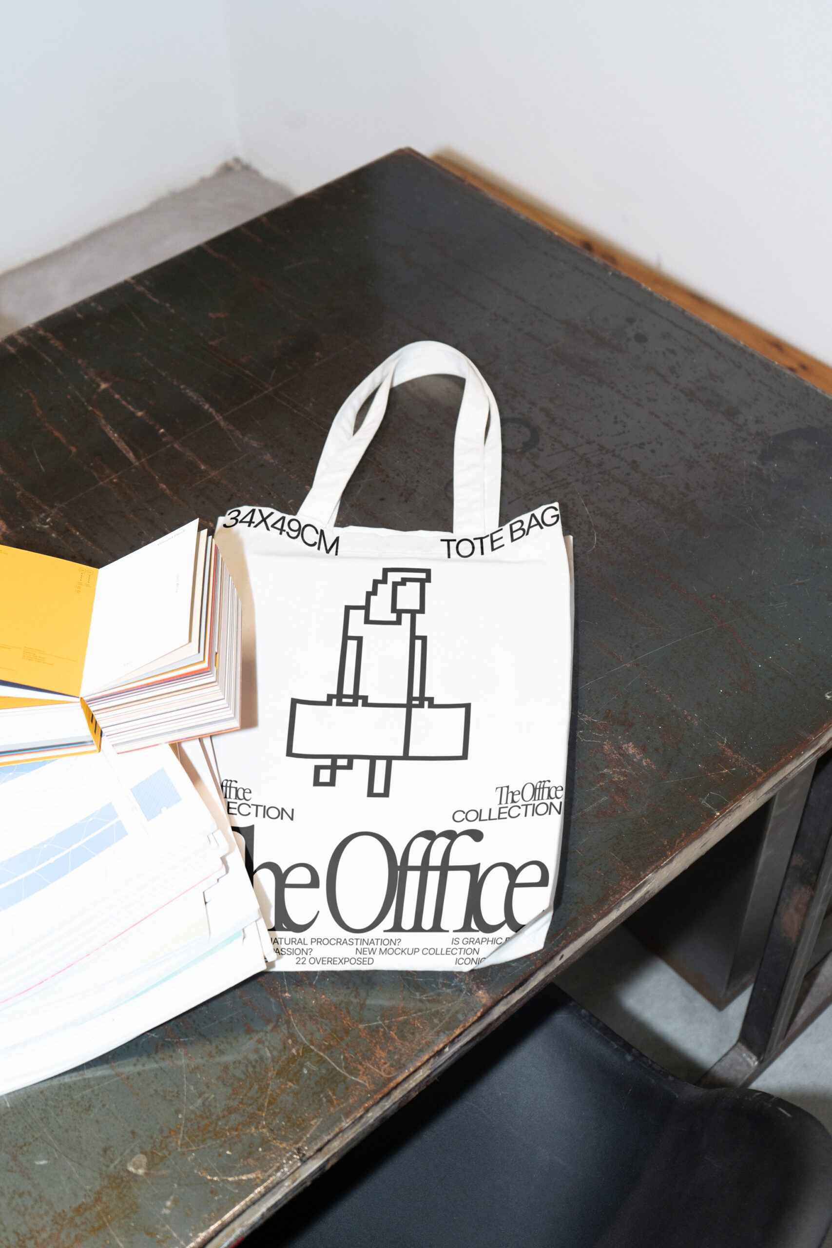 Tote bag mockup on top a brown metal table next to an open book and magazines
