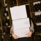 PSD mockup of a woman holding a pile of cardboard boxes. The boxes are rectangular and are place in the interior of a wine cellar. Wine packaging mockup. Wine shop mockup. Restaurant mockup.