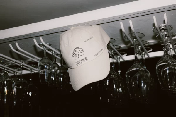 Hat PSD mockup. Cap PSD mockup. White hat mockup hanging from a shelf surrounded by crystal glasses. Wine merchandising mockup. Restaurant merchandising mockup. Fashion and apparel mockup.