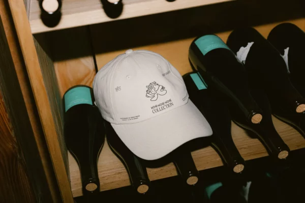 Hat PSD mockup. Cap PSD mockup. White hat mockup placed on a shelf surrounded by several wine bottles. Wine merchandising mockup. Restaurant merchandising mockup. Fashion and apparel mockup.