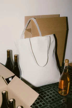 White tote bag PSD mockup. Tote bag mockup surrounded by wine bottles and cardboard boxes. Wine merchandising mockup. Restaurant mockup. Wine bar mockup. Fashion and apparel mockup.