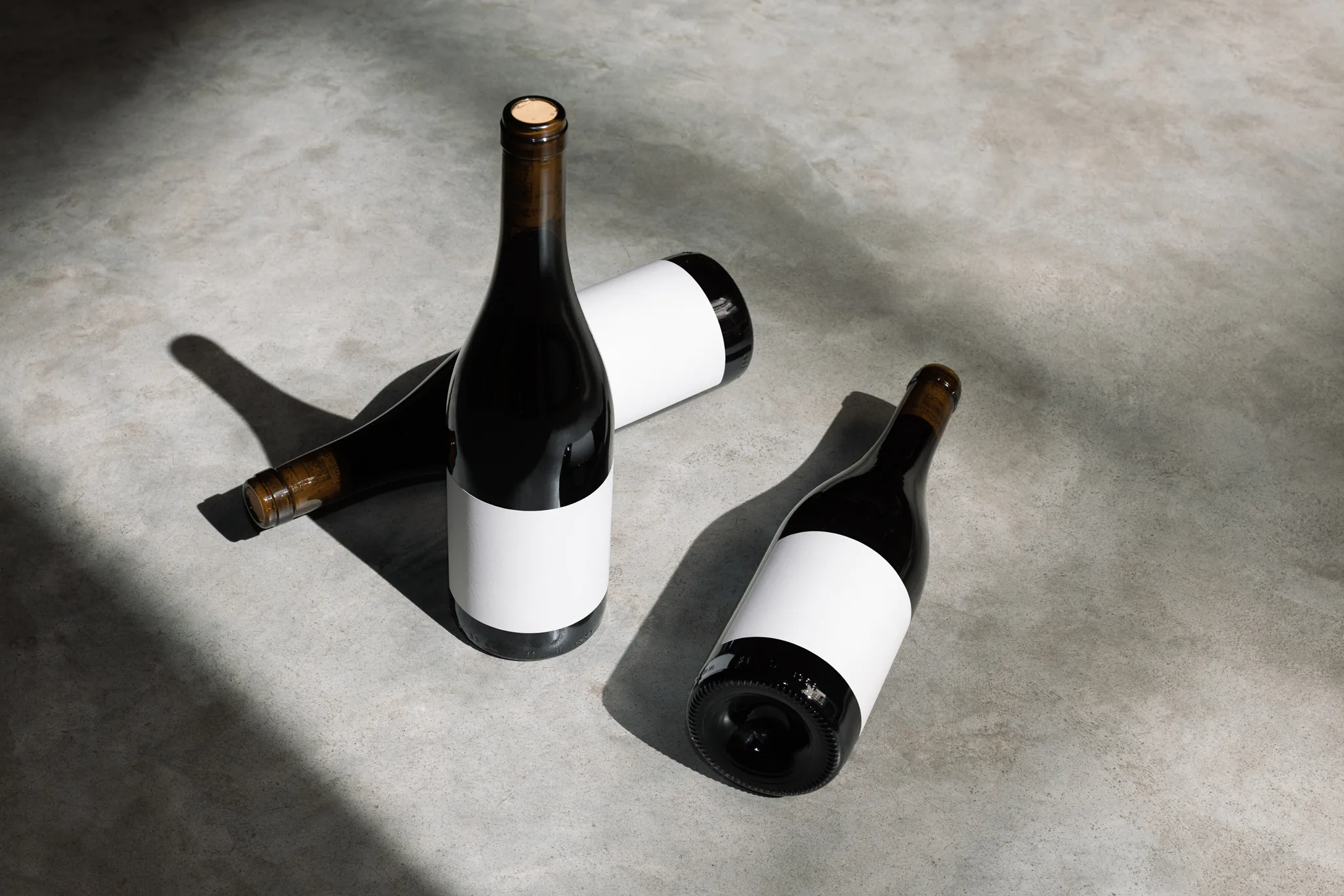 Wine label PSD mockup. Wine bottle mockup placed on a concrete floor. Three wine bottles placed in different positions, with a ray of light resting on them. Wine packaging mockup. Restaurant mockup. Wine bar mockup.