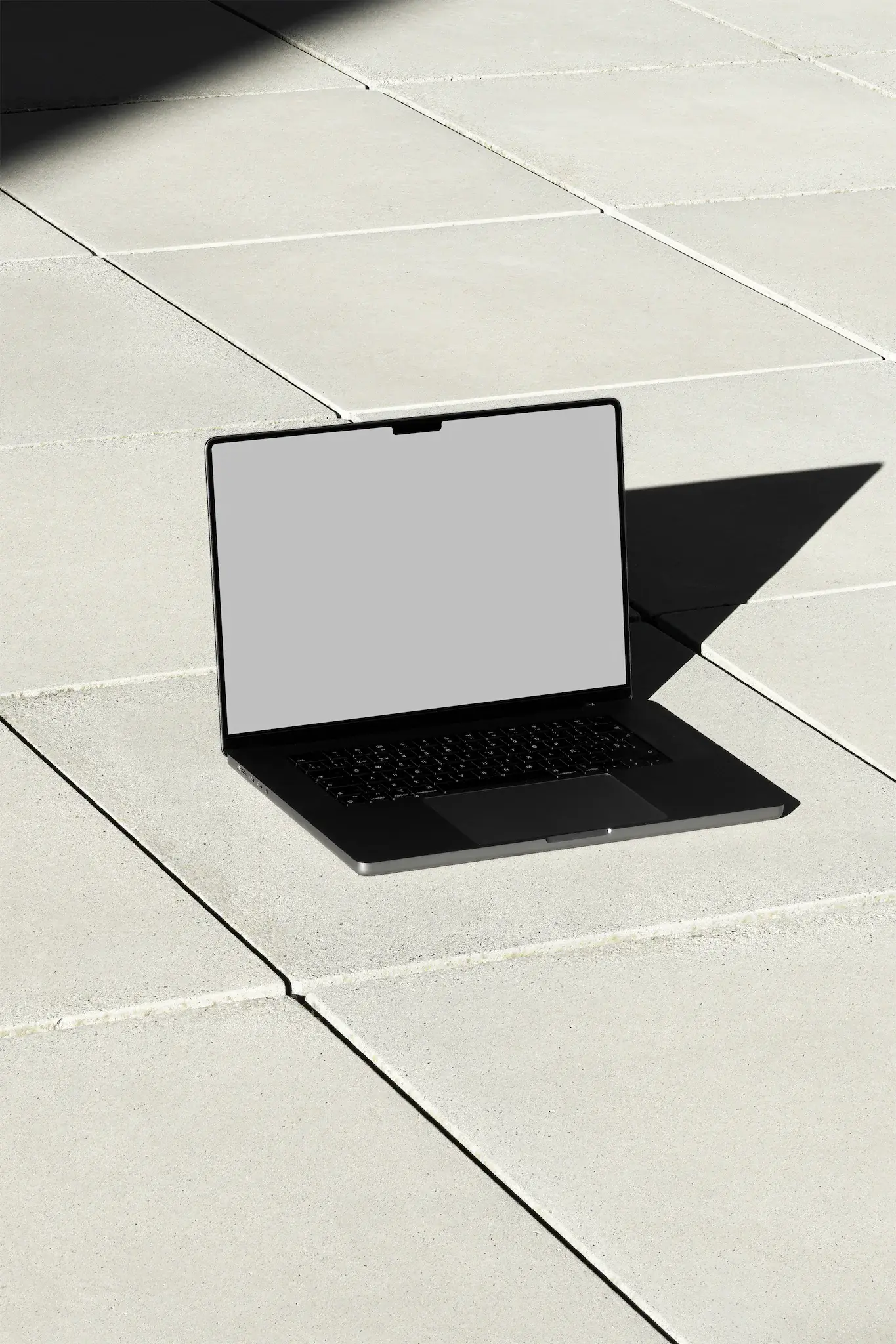 Macbook Pro PSD mockup on top of a floor of concrete slabs with real lights and shadows. Tech mockup.