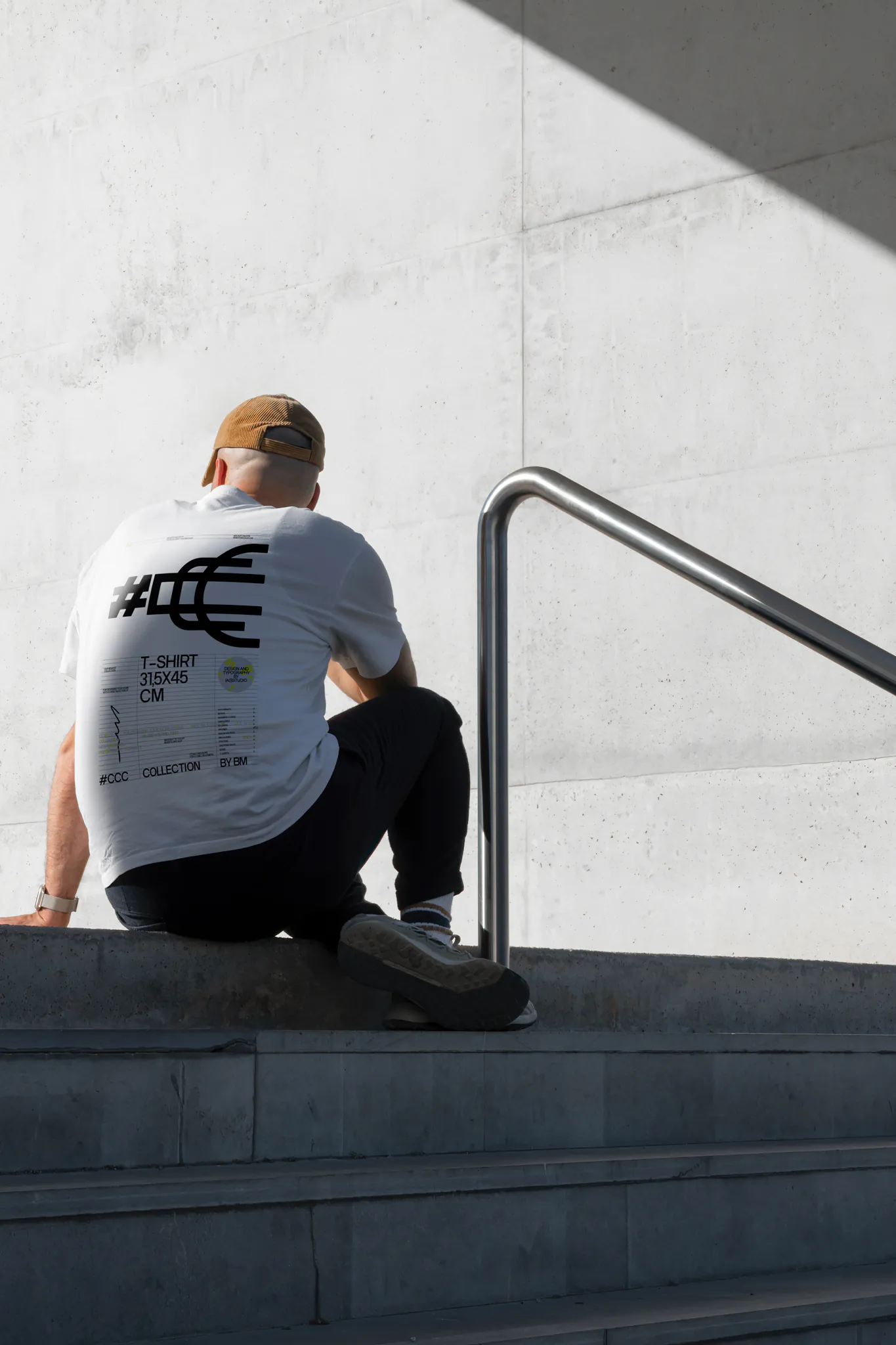 White t-shirt back PSD mockup. T-shirt mockup being worn by a man who is sitting on concrete stairs in a concrete scene. Fashion and apparel mockup.