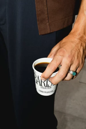 Disposable coffee cup mockup being grabbed by the hand of a man. Coffee cup mockup being held by a human, wearing modern and contemporary clothes. Hand holding cardboard coffee cup mockup, paper cup mockup, tea cup mockup, high quality mockup, PSD file.