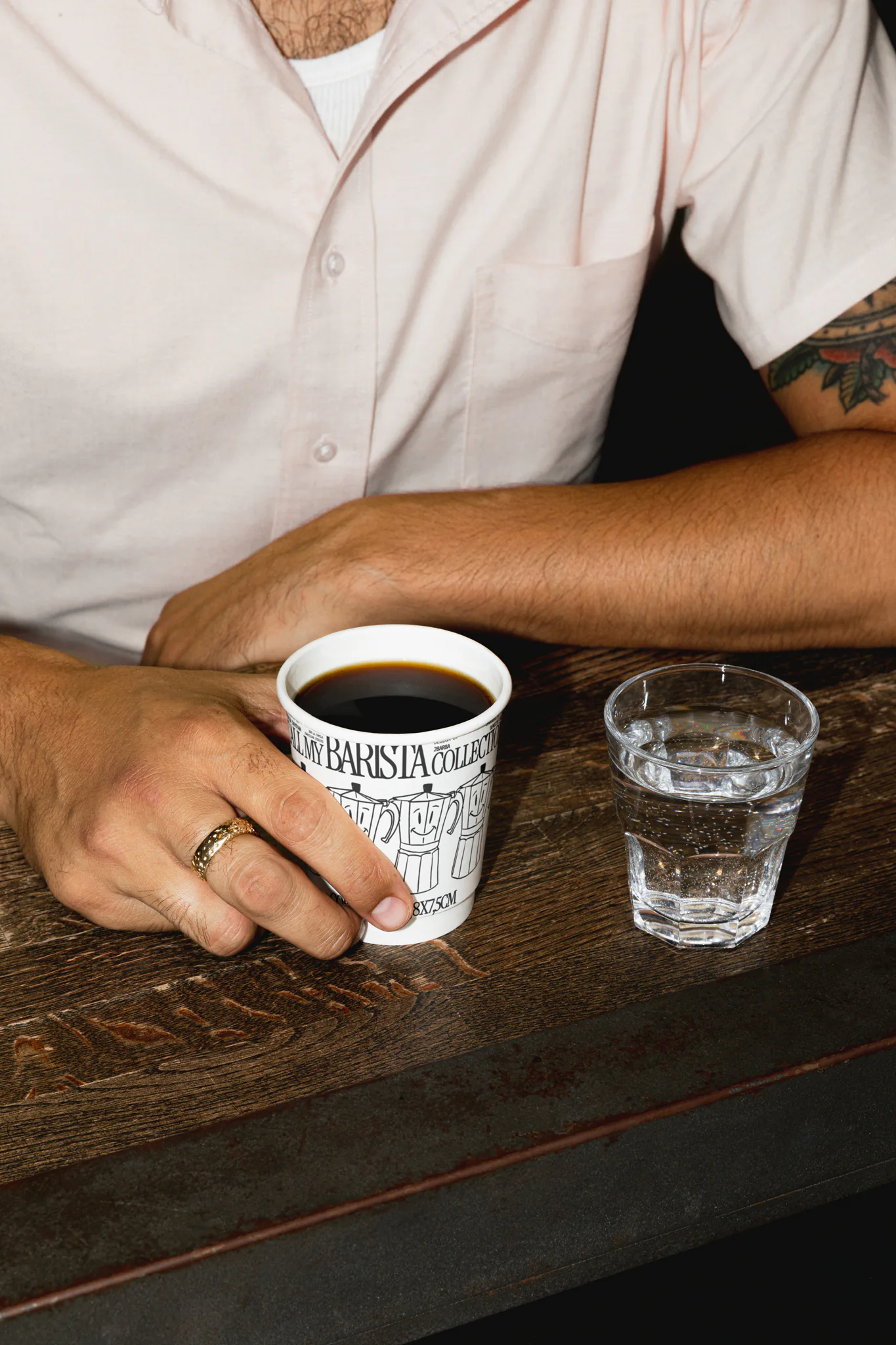 Hand holding white coffee cup mockup in a coffee shop. Coffee cup mockup being grabbed by a man, wearing a beige t-shirt. Hand holding cardboard coffee cup mockup, paper cup mockup, tea cup mockup, high quality mockup, PSD file.