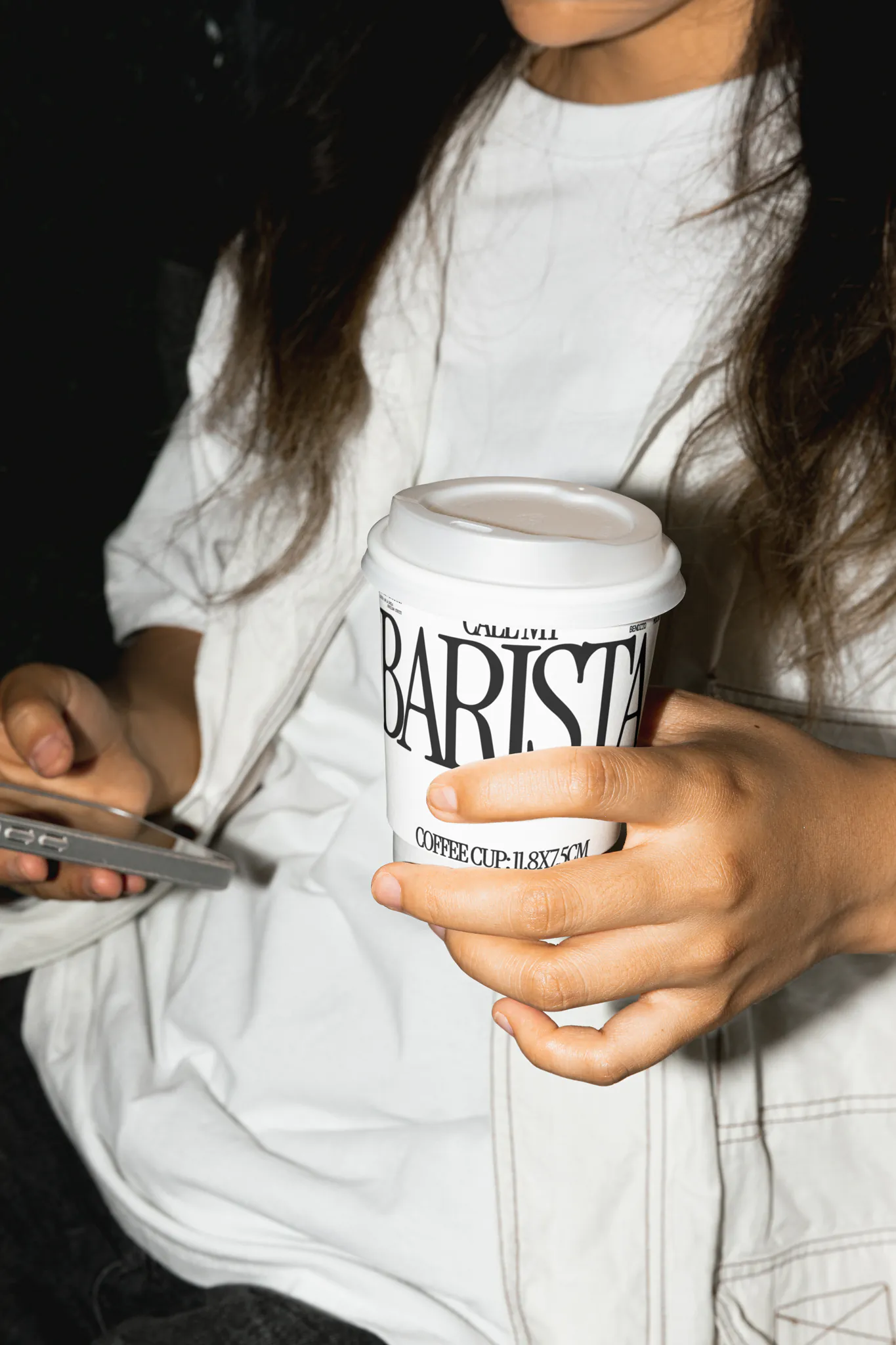 Female hand holding a coffee cup mockup in a coffee shop. Coffee cup mockup being grabbed by a girl, wearing street-style clothes. Hand holding cardboard coffee cup mockup, paper cup mockup, tea cup mockup, high quality mockup, PSD file.