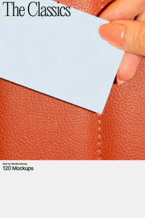 A close-up of a hand with glossy peach-colored nails holding a blank light blue business card against a textured orange leather background.