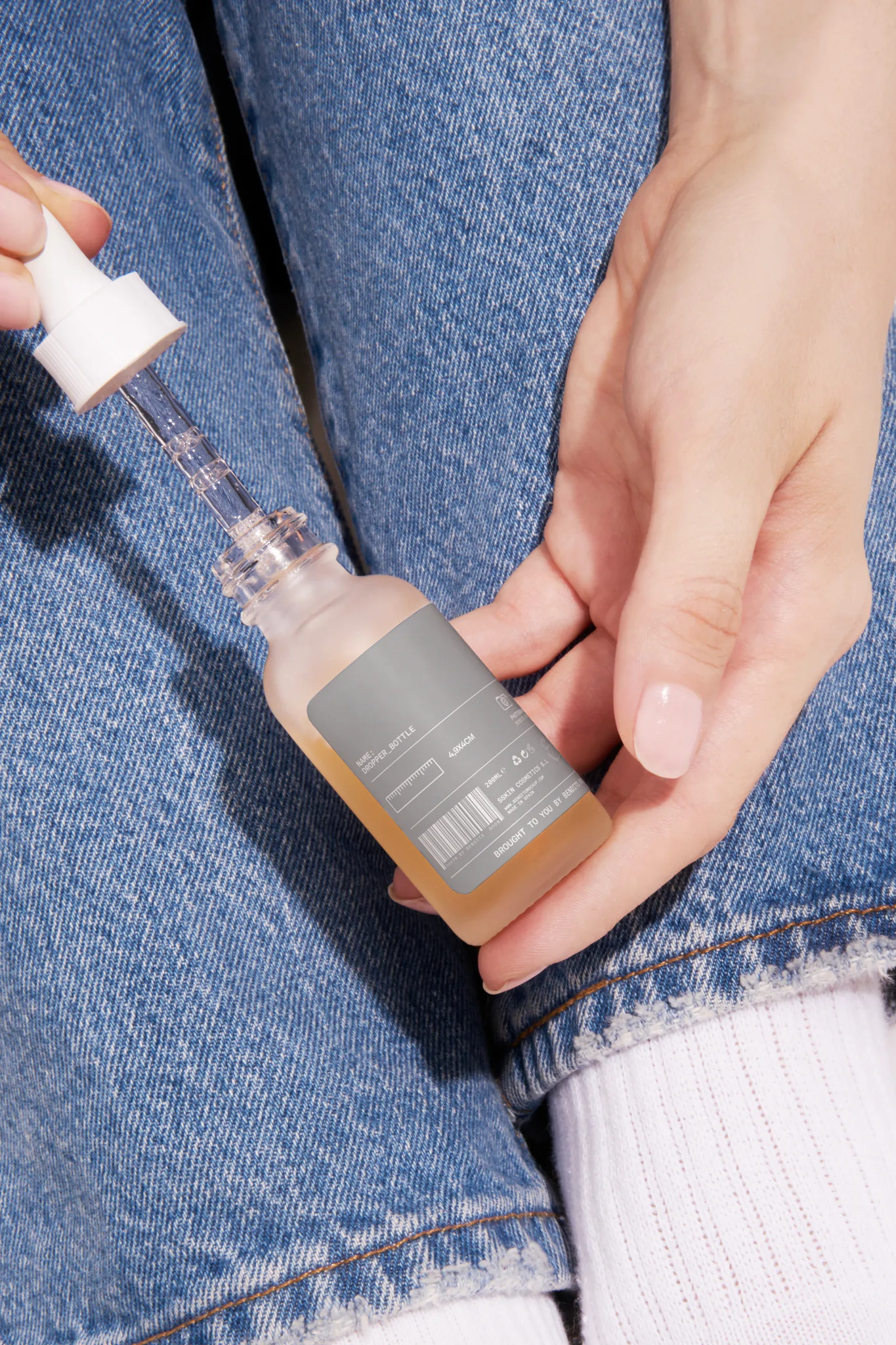 Woman with jeans holding a dropper bottle mockup. Skin care packaging mockup. Skin care PSD file. High-quality dropper bottle mockup.