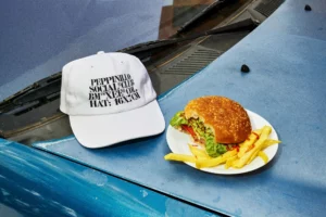 Hat mockup next to a plate with a hamburger and fries over the hood of a blue car in a burger restaurant parking. Clothing mockup. Hat PSD file. Cap mockup. Premium quality hat mockup. PSD premium editable file.