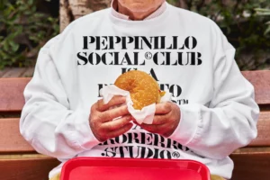 Sweatshirt mockup worn by an old person who is eating a burger sitting outside on the bench of a burger restaurant. Clothing mockup. Jumper mockup. Takeaway PSD file. Takeaway mockup. Fast food mockup. Premium quality sweatshirt mockup. Takeaway PSD high-quality editable file. Burger high-quality mockup.