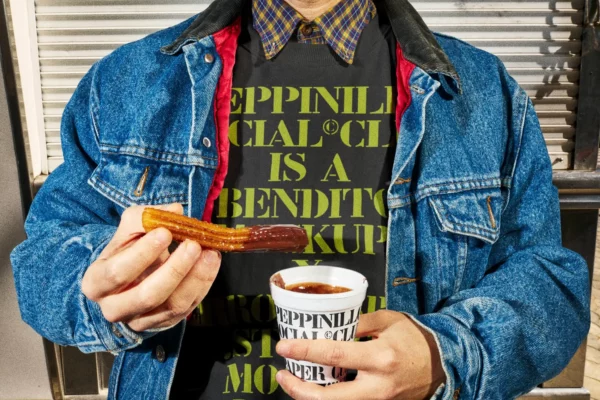 Sweatshirt mockup worn by a young guy in a burger place who is eating a long fritter with chocolate. Clothing mockup. Jumper mockup. Takeaway PSD file. Takeaway mockup. Fast food mockup. Premium quality jumper mockup. Takeaway PSD high-quality editable file. Burger high-quality mockup.