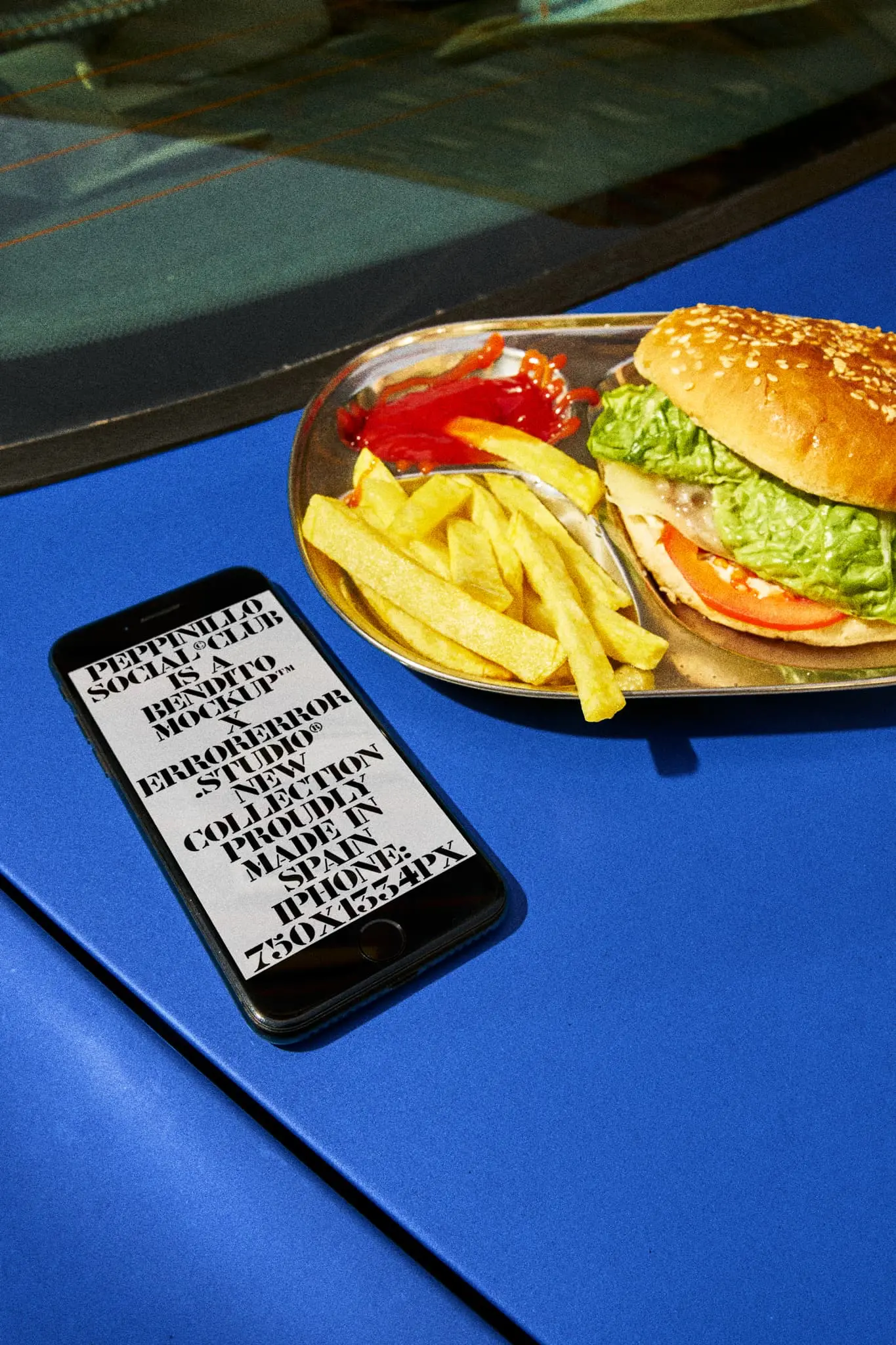 iPhone mockup next to a plate with a hamburger and fries over the hood of a blue car in the parking of a take-away restaurant. Device mockup. iPhone PSD file. Premium quality iPhone mockup. iPhone PSD high-quality editable file.
