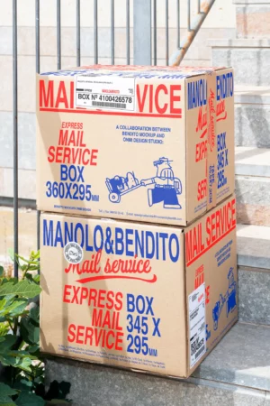 Free aesthetic delivery mockup of two square boxes with editable tape and stickers piled up outside. Free high-quality box mockup for your product branding. Free box mockup. Premium cardboard box mockup with editable components in an outdoors setting created for Adobe Photoshop.