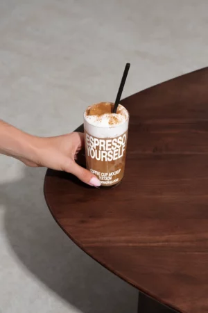 Hand holding an Espresso Yourself cup with a frothy coffee drink